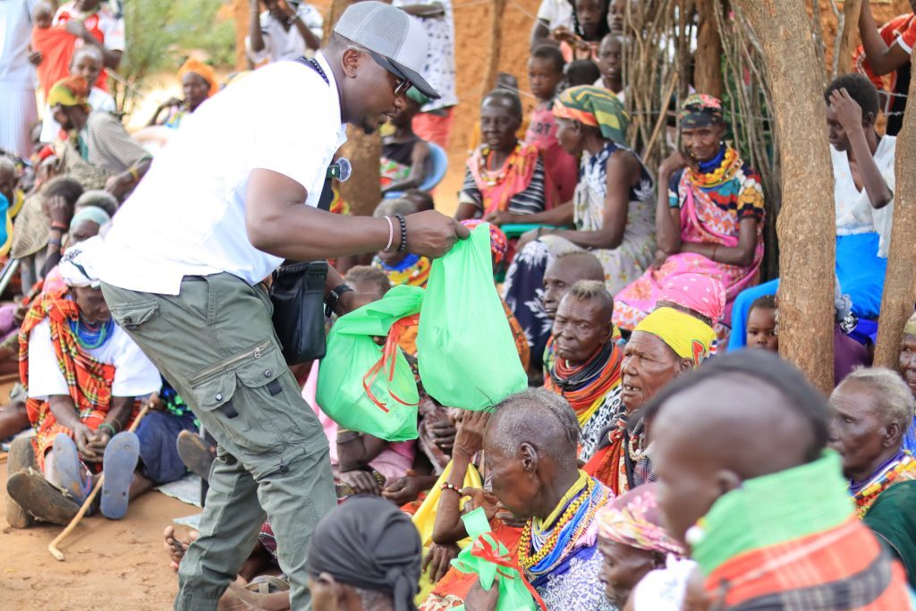 A Lusega Tales team member handing out bags of supplies to seated elders